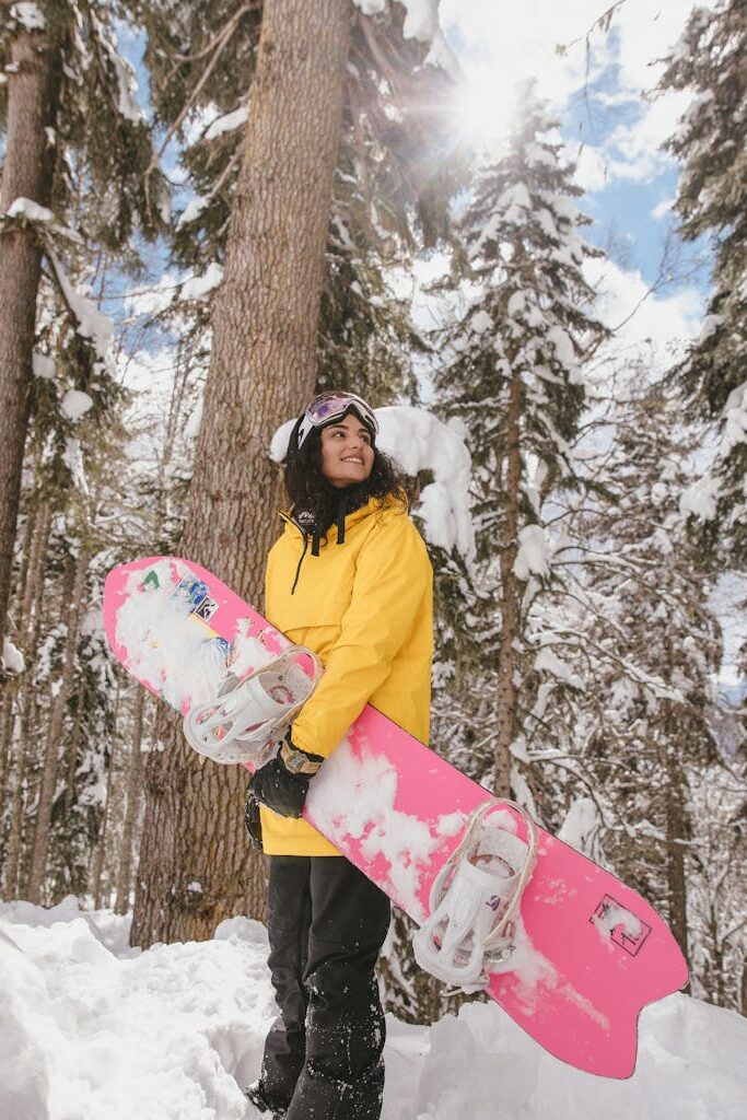 A Woman in Yellow Jacket Standing on a Snow Covered Ground while Holding a Snowboard